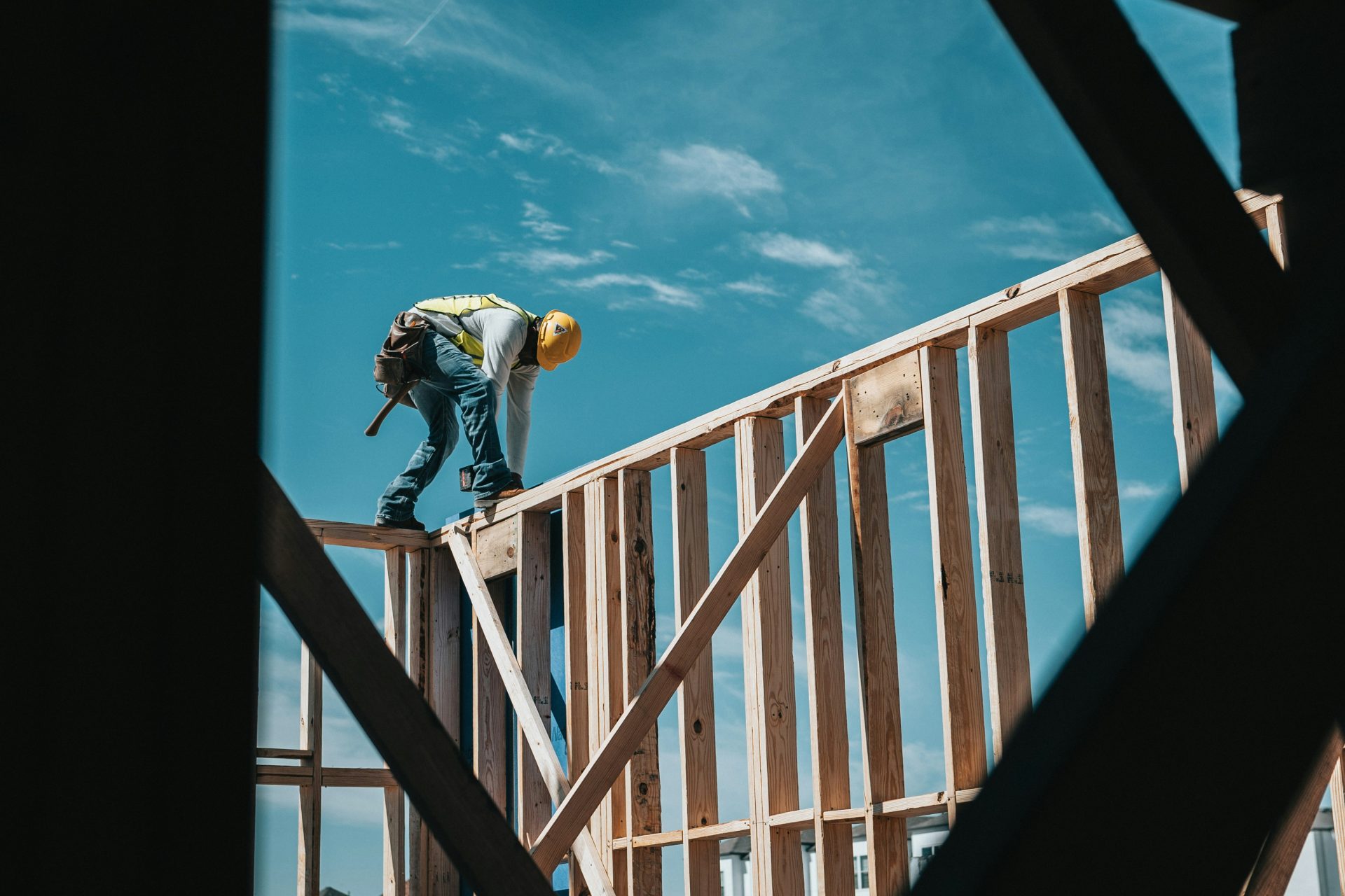 Worker balancing on wooden house framework.