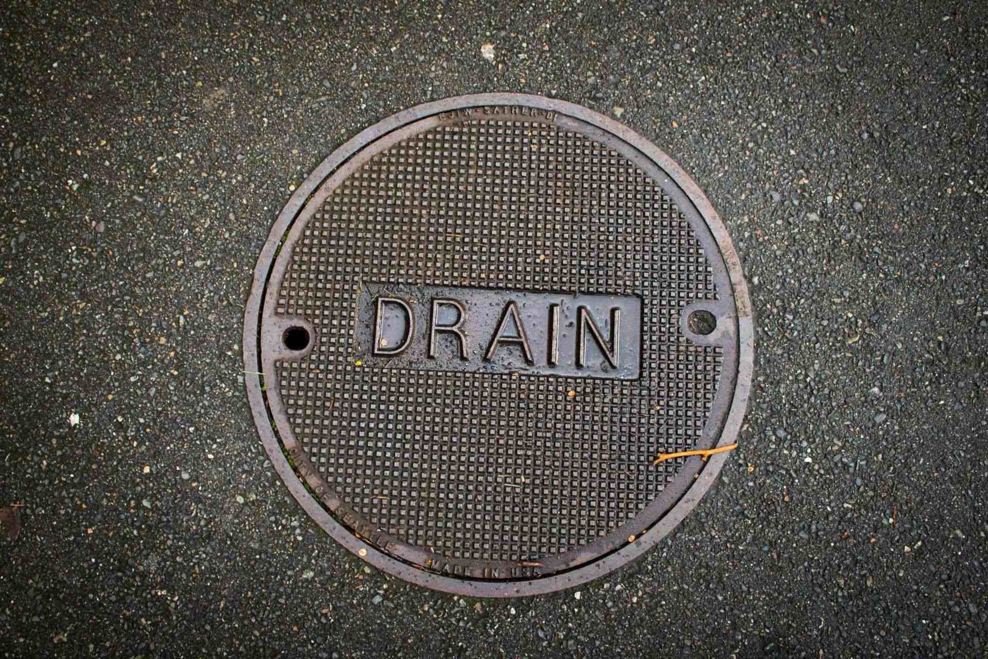 Manhole cover labeled 'DRAIN' on asphalt ground.